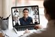 Eine Frau sitzt am Schreibtisch und schaut auf einen Computer-Bildschirm auf dem mehrere Teilnehmer*innen per webcam teilnehmenIndian ethnicity young woman lead video call distant chat, group of different mates using videoconference