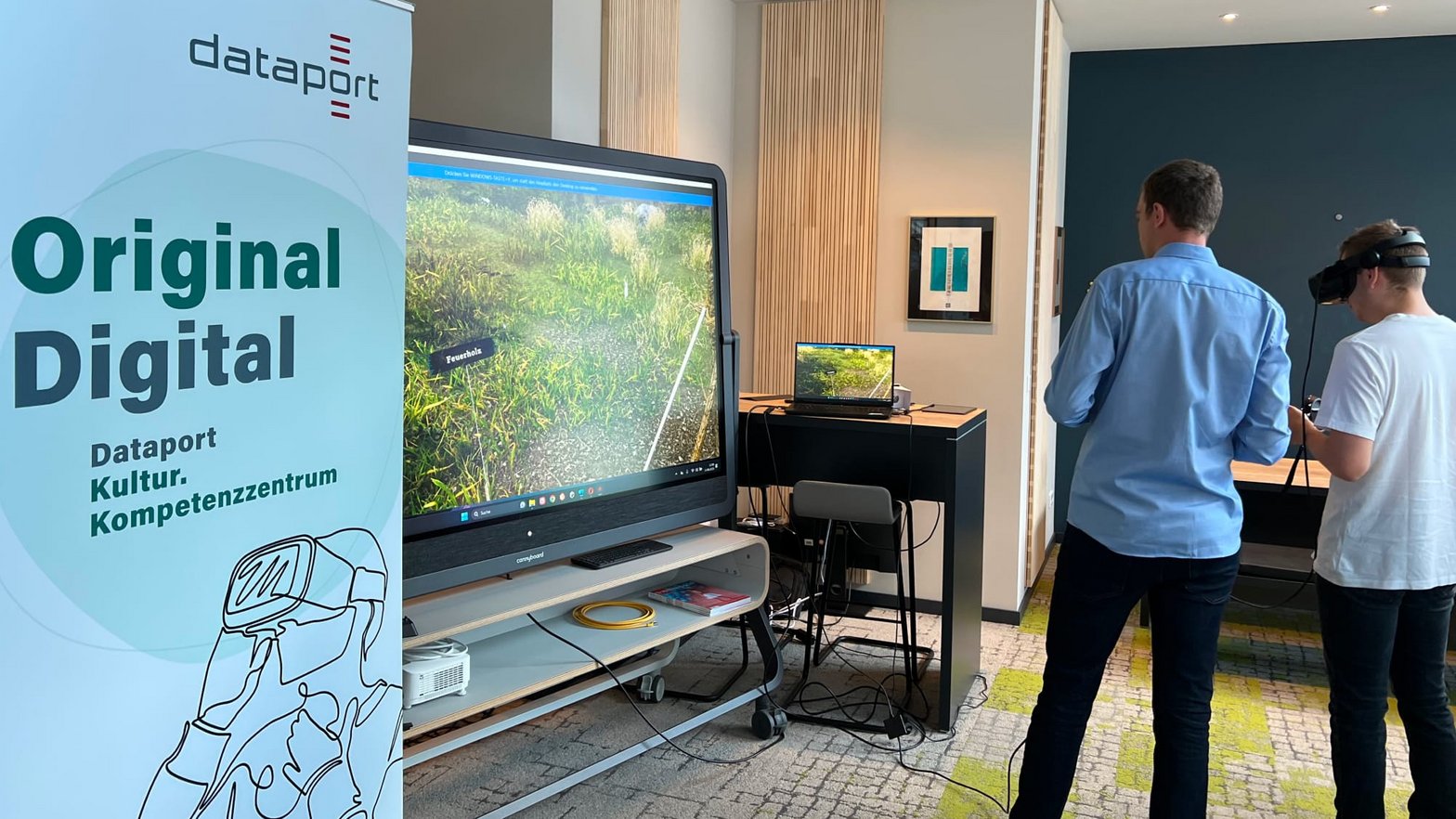 Im Digital Hub Einbeck: Zwei Personen stehen vor einem großen Bildschirm. Einer trägt eine VR-Brille. 