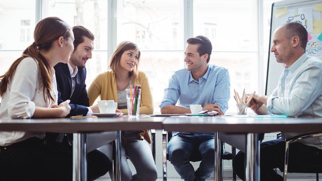 Fünf Menschen sitzen um einen runden Tisch und tauschen sich aus