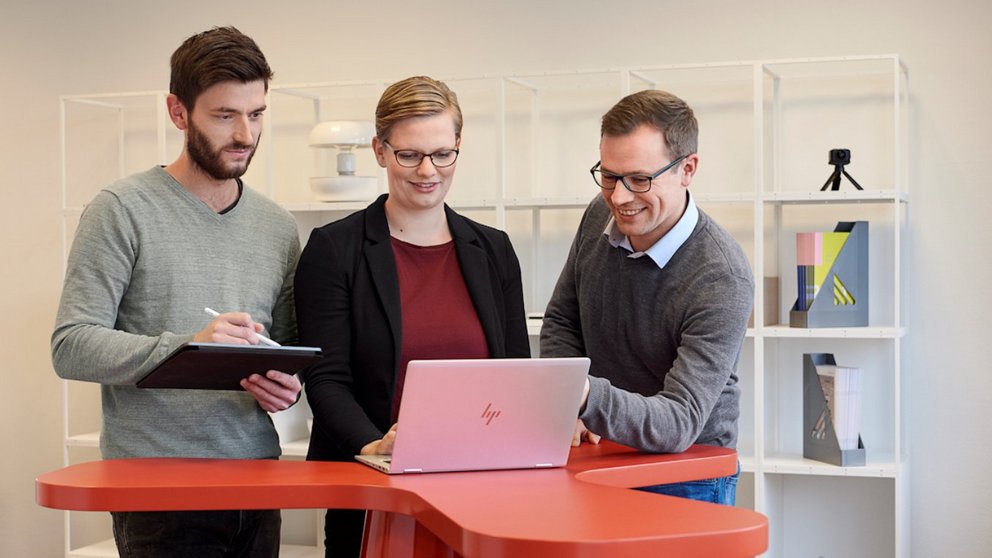 Drei Personen blicken auf Laptop und tauschen sich aus