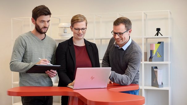 Drei Personen blicken auf Laptop und tauschen sich aus