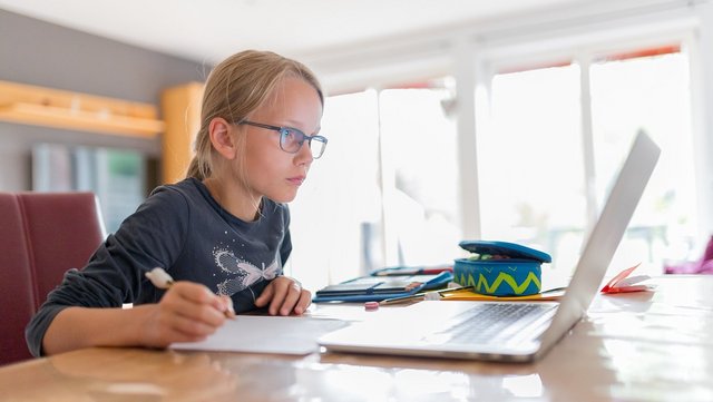 Ein junges Mädchen erledigt Schulfaufgaben am Laptop und macht sich Notizen.