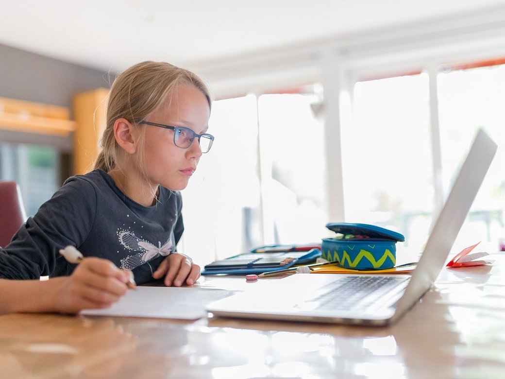 Ein junges Mädchen erledigt Schulfaufgaben am Laptop und macht sich Notizen.