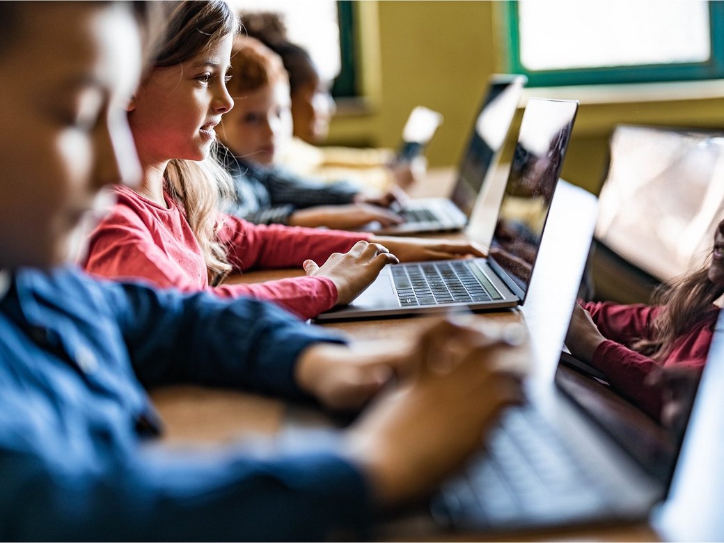 Mehrere Kinder sitzen im Klassenraum und arbeiten an Laptops. 